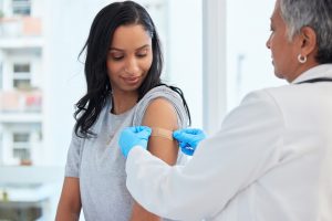 Healthcare, woman and doctor with plaster, vaccination and consultation in a hospital, cure and disease. Female patient, client and medical professional with band aid, care and injection for safety