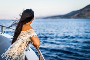 A woman stands at the railing of a cruise ship looking out at the water